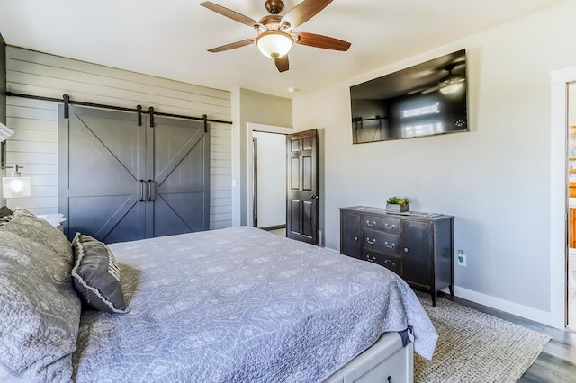bedroom with wood finished floors, a barn door, wooden walls, a ceiling fan, and baseboards