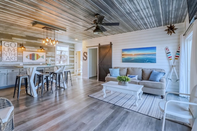 living area with wood finished floors, a barn door, wooden ceiling, wooden walls, and a ceiling fan