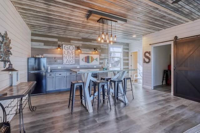 dining area featuring dark wood finished floors, wood ceiling, wooden walls, and a barn door