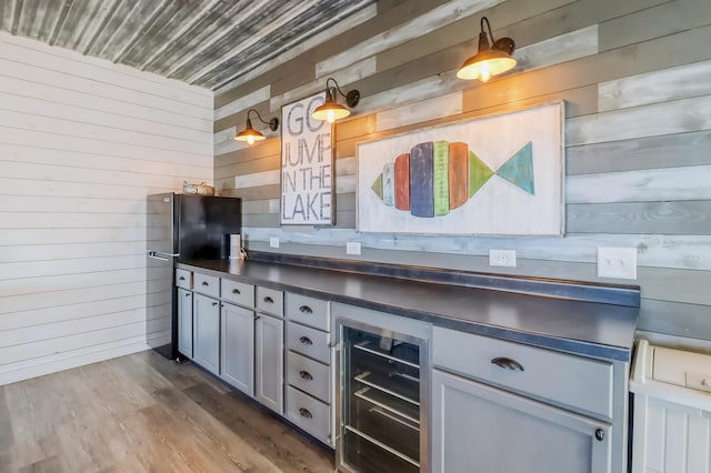 kitchen featuring freestanding refrigerator, beverage cooler, wood walls, and dark countertops
