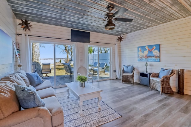living room with wooden walls, a ceiling fan, and wood finished floors