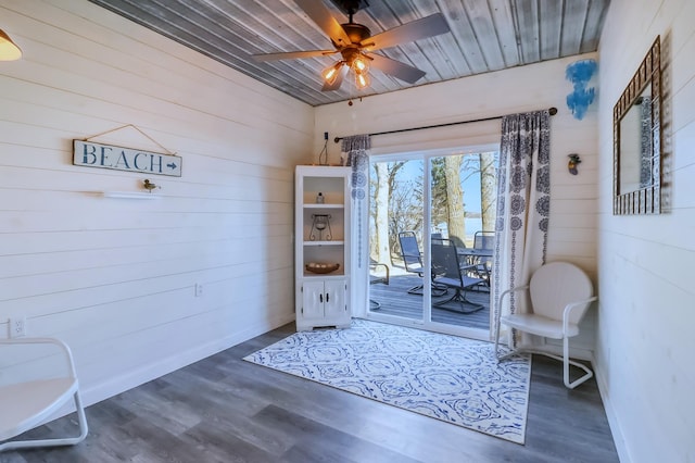 interior space with wooden walls, a ceiling fan, and dark wood finished floors