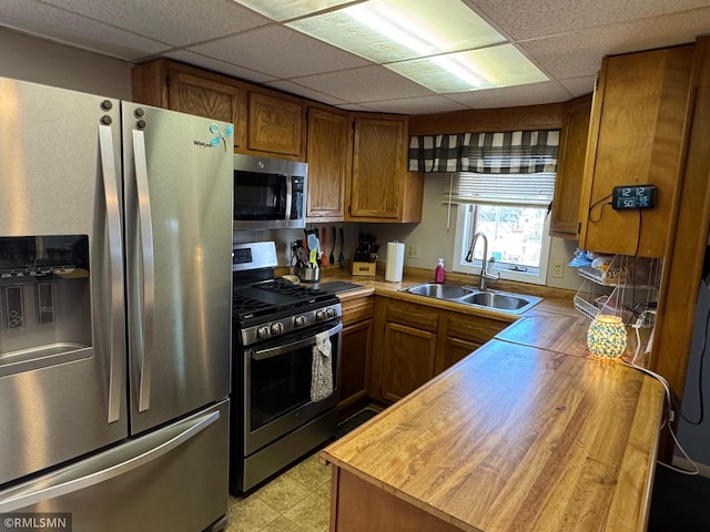 kitchen featuring wooden counters, a drop ceiling, a sink, appliances with stainless steel finishes, and brown cabinets