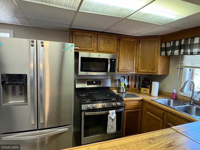 kitchen featuring a sink, light countertops, a paneled ceiling, appliances with stainless steel finishes, and brown cabinets