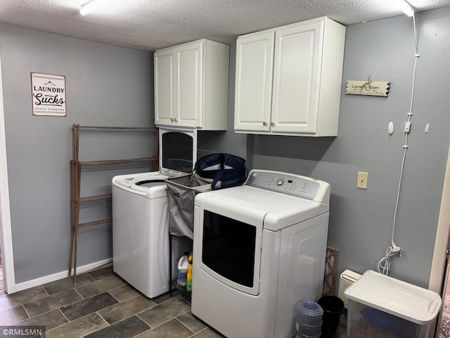 washroom featuring cabinet space, washer and dryer, a textured ceiling, and baseboards
