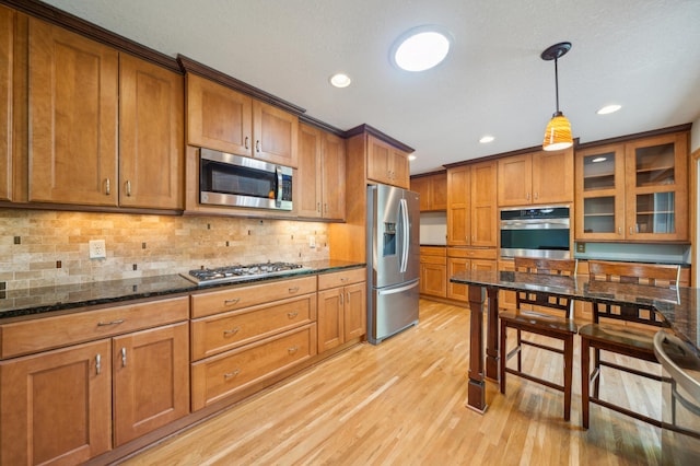 11413 Christansen Ct, Burnsville, MN 55337 - kitchen featuring stainless steel appliances, brown cabinetry, light wood-type flooring, dark stone counters, and hanging light fixtures