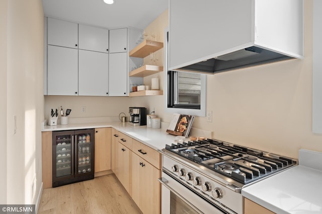 kitchen featuring light brown cabinetry, stainless steel gas range, custom exhaust hood, light wood finished floors, and beverage cooler