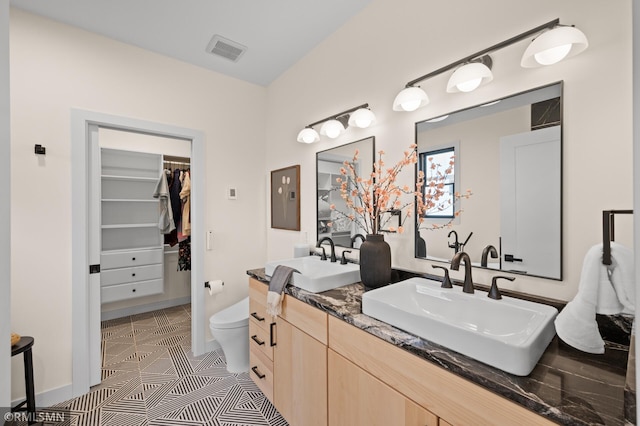 full bath with visible vents, a sink, a walk in closet, and toilet