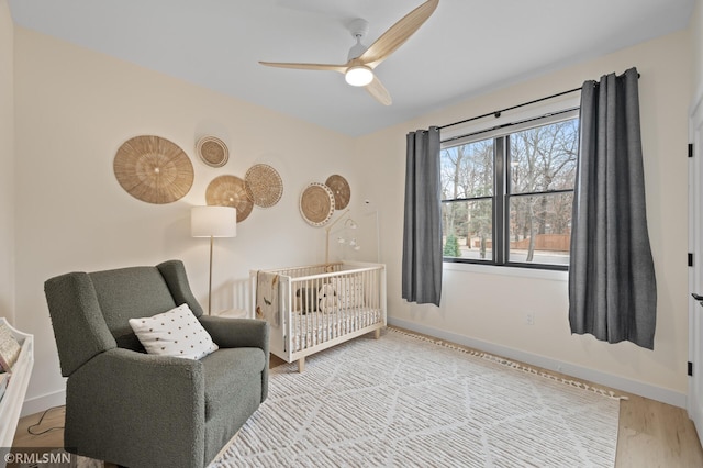 bedroom featuring baseboards, ceiling fan, a crib, and wood finished floors