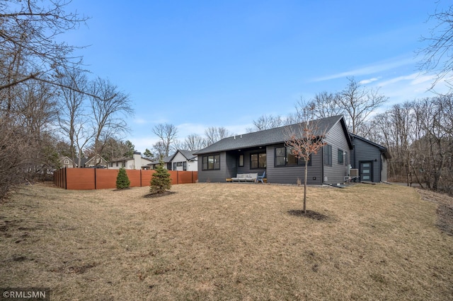 rear view of property featuring fence, a shingled roof, and a yard