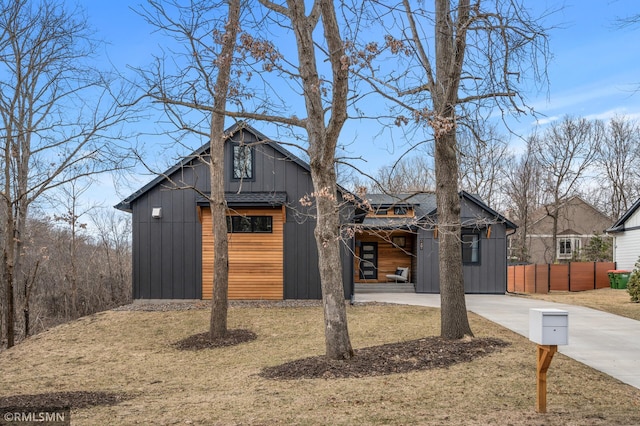 view of front of home with board and batten siding, fence, concrete driveway, and a front lawn