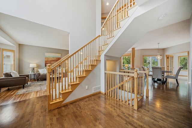 stairway featuring a towering ceiling, visible vents, wood finished floors, baseboards, and recessed lighting