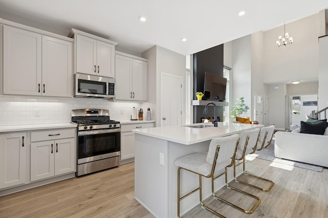 6767 Bluestem Way, Minnetrista, MN 55331 - kitchen featuring appliances with stainless steel finishes, open floor plan, light wood-style flooring, tasteful backsplash, and light countertops