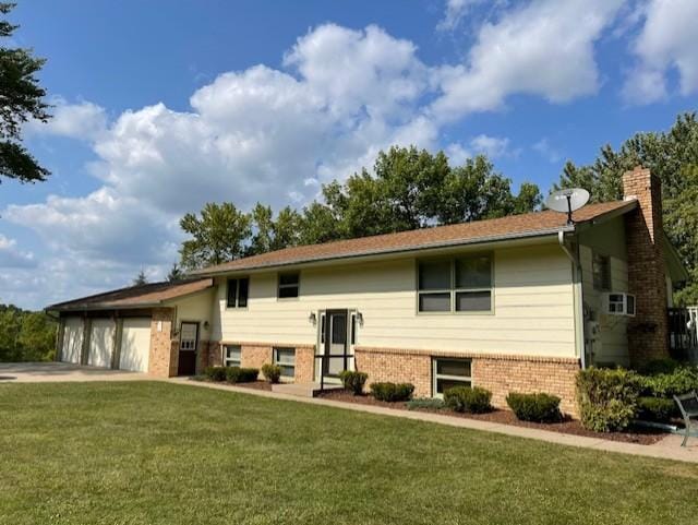 split foyer home with a chimney, a front yard, an attached garage, and brick siding