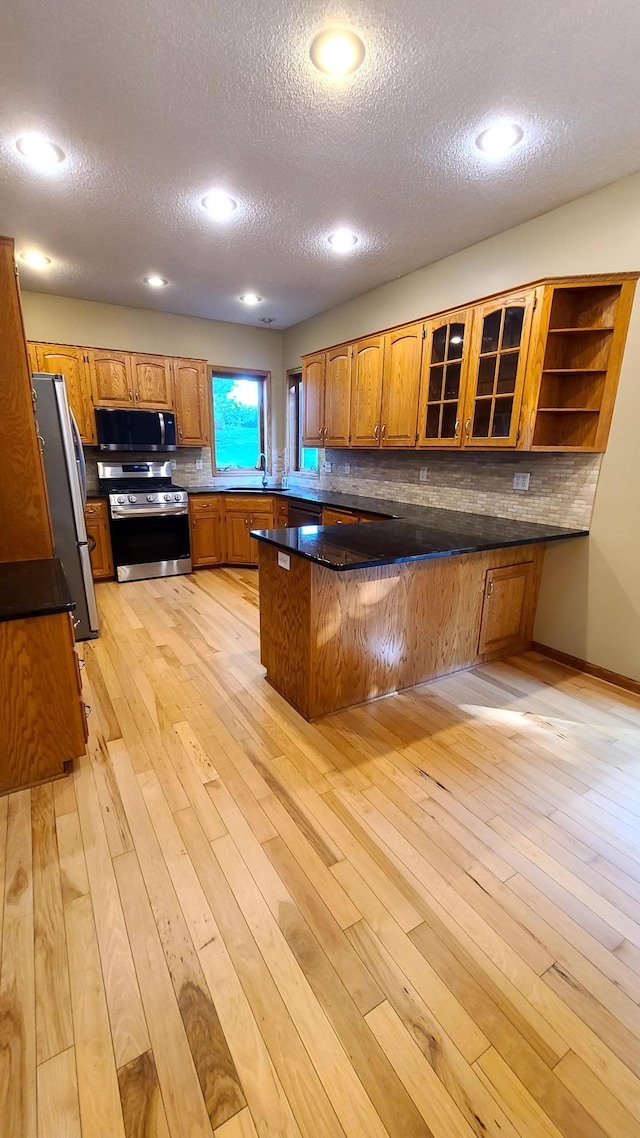 1404 19th Ave NW, Faribault, MN 55021 - kitchen featuring a peninsula, appliances with stainless steel finishes, brown cabinets, a textured ceiling, and tasteful backsplash