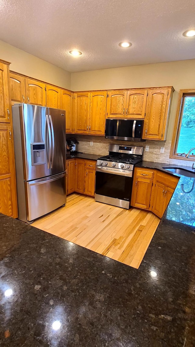 1404 19th Ave NW, Faribault, MN 55021 - kitchen with appliances with stainless steel finishes, decorative backsplash, brown cabinetry, and dark stone countertops