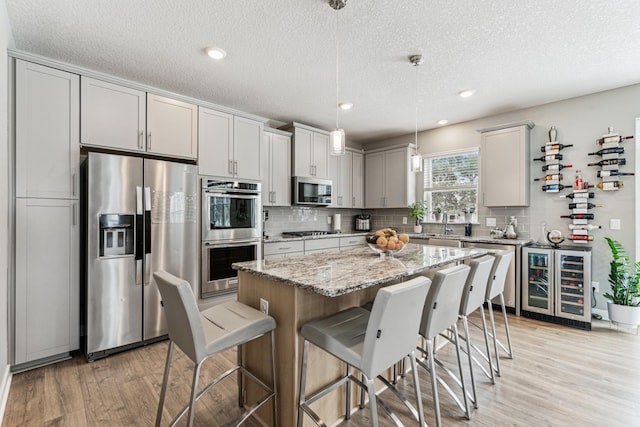12972 Bauer Dr N, Champlin, MN 55316 - kitchen with appliances with stainless steel finishes, beverage cooler, light wood-style flooring, decorative backsplash, and a breakfast bar