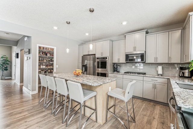 12972 Bauer Dr N, Champlin, MN 55316 - kitchen featuring appliances with stainless steel finishes, a kitchen island, decorative backsplash, light wood-style floors, and a breakfast bar area
