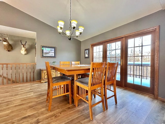 dining space with a notable chandelier, vaulted ceiling, plenty of natural light, and wood finished floors