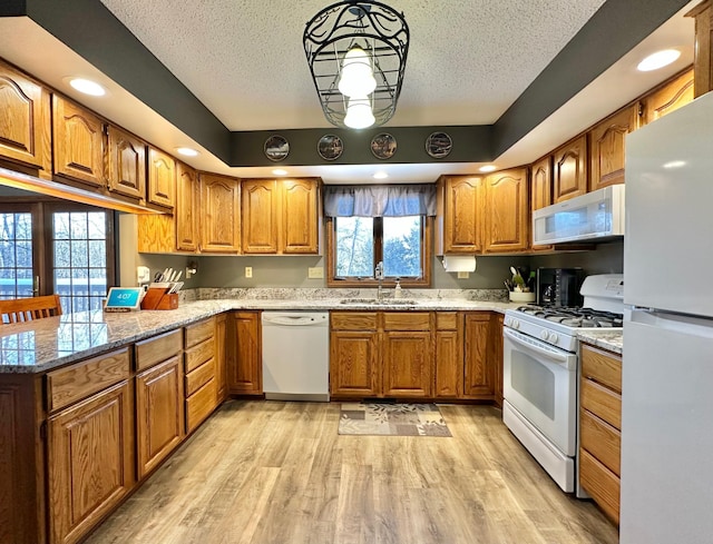 kitchen featuring white appliances, a textured ceiling, brown cabinets, a sink, and light wood-style flooring