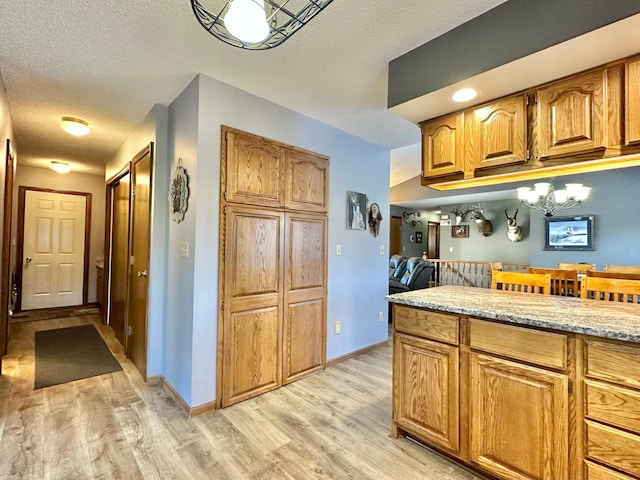 kitchen featuring baseboards, light countertops, a textured ceiling, brown cabinets, and light wood-style flooring