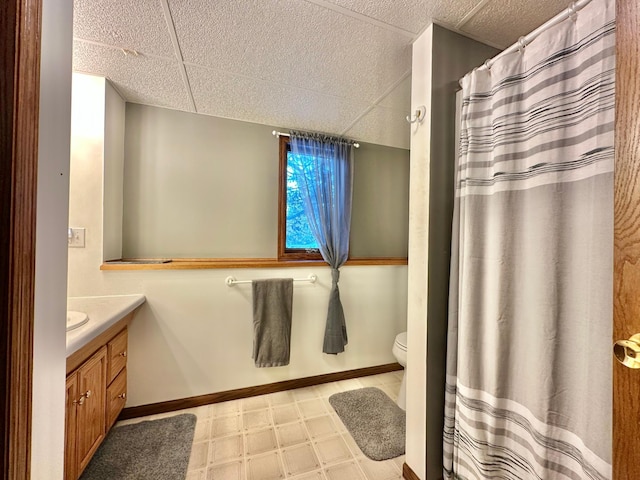 bathroom with vanity, toilet, tile patterned floors, baseboards, and a drop ceiling