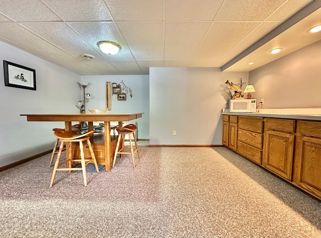 bar featuring baseboards, white microwave, and a drop ceiling