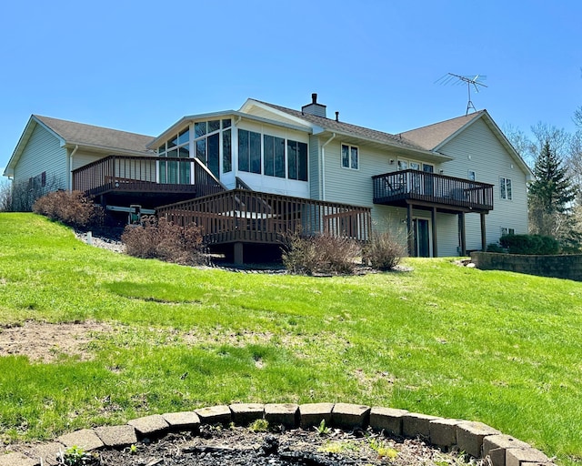 back of property with a sunroom, a wooden deck, a chimney, and a yard