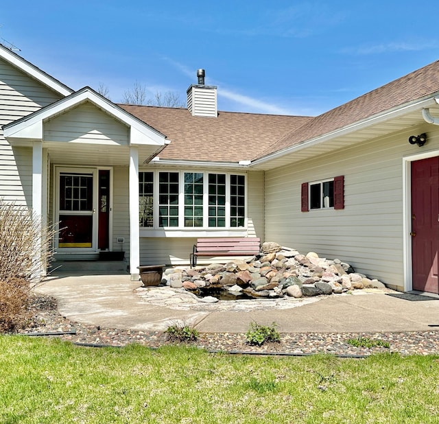 entrance to property with a shingled roof and a chimney