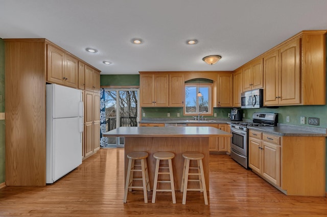 kitchen featuring a sink, light wood-type flooring, a breakfast bar area, a kitchen island, and appliances with stainless steel finishes