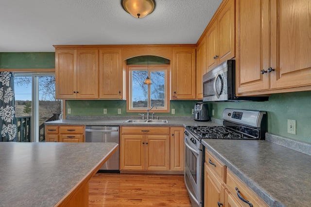 kitchen with a sink, stainless steel appliances, light wood-style floors, dark countertops, and a textured ceiling