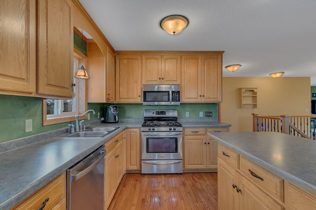 kitchen with a sink, dark countertops, light brown cabinets, stainless steel appliances, and light wood finished floors