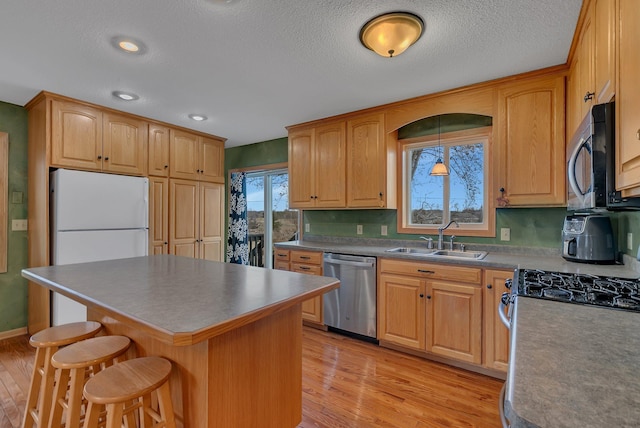 kitchen featuring light wood-style flooring, a breakfast bar, stainless steel appliances, a kitchen island, and a sink