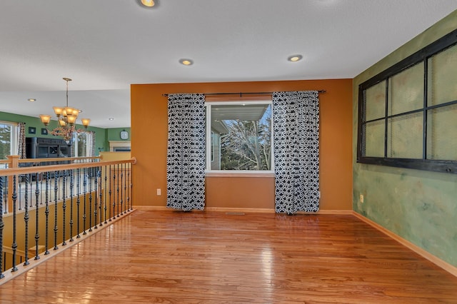 unfurnished room featuring an inviting chandelier, wood finished floors, and baseboards