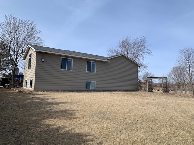 view of home's exterior featuring a lawn, a shingled roof, and fence