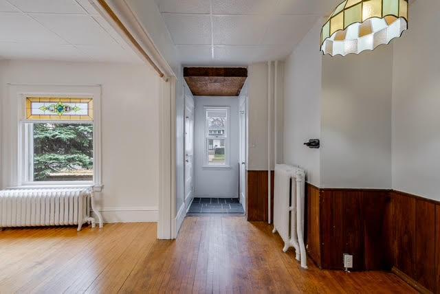 doorway to outside featuring wood finished floors, radiator heating unit, and a wainscoted wall