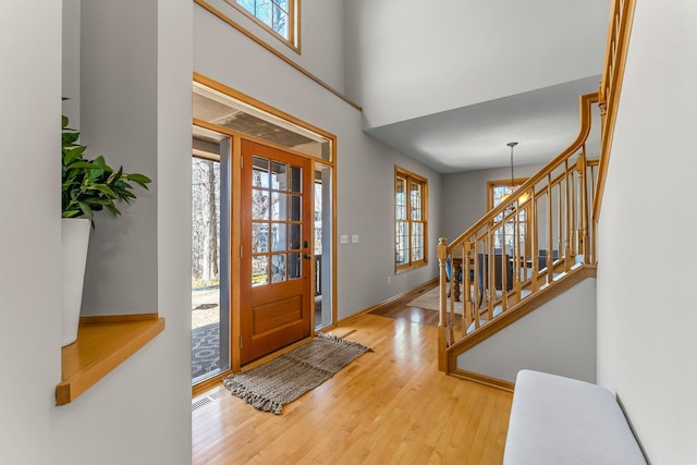 entryway featuring a towering ceiling, baseboards, stairway, visible vents, and wood finished floors