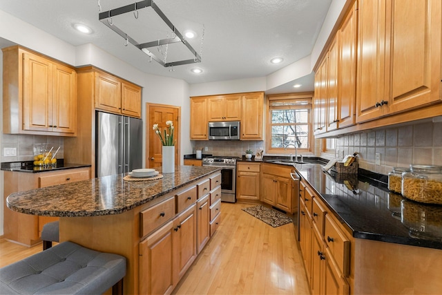 kitchen with light wood-type flooring, a sink, backsplash, and appliances with stainless steel finishes
