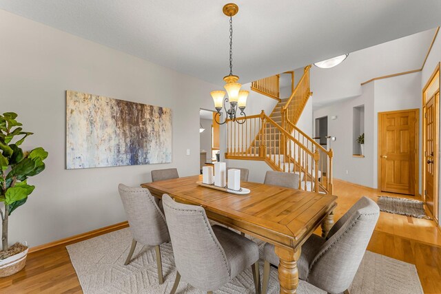 dining space featuring baseboards, stairway, a chandelier, and wood finished floors