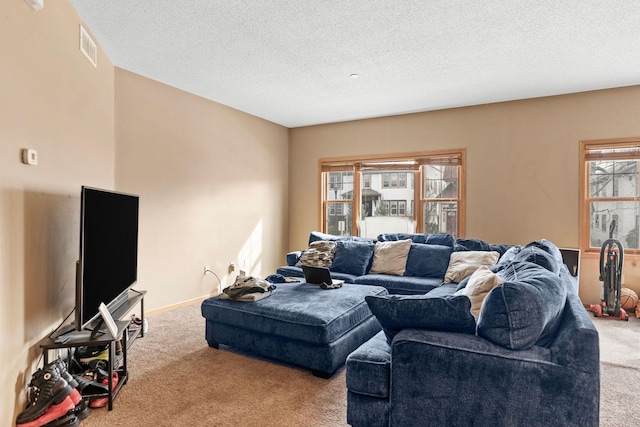 carpeted living area featuring baseboards, a textured ceiling, and visible vents