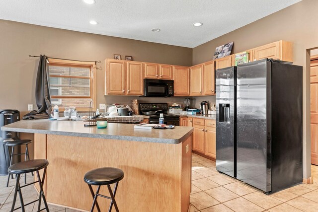 kitchen featuring a breakfast bar area, black appliances, and light brown cabinetry
