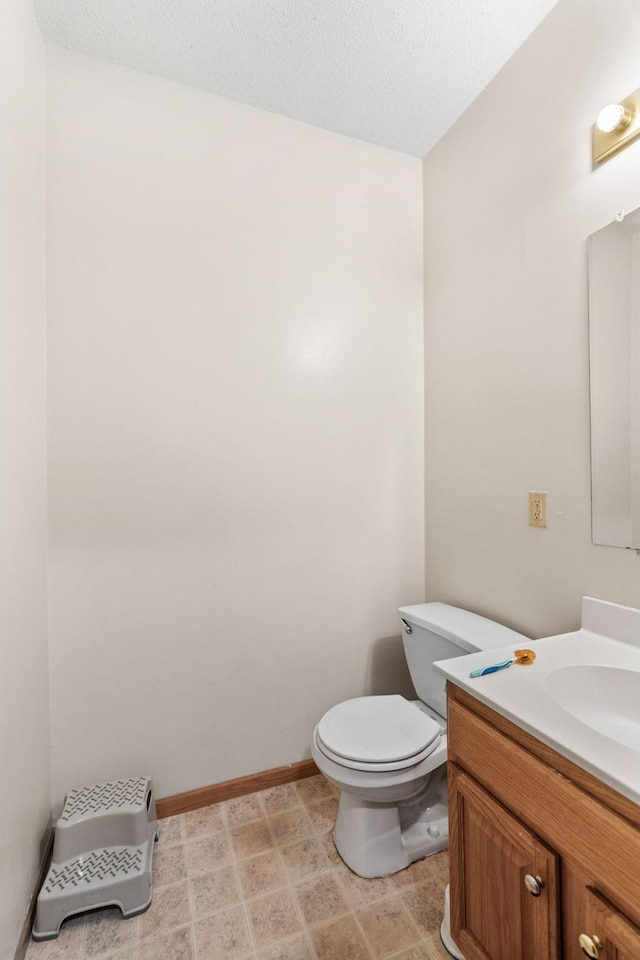 bathroom featuring baseboards, toilet, vanity, and a textured ceiling