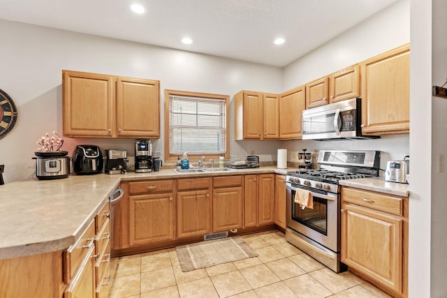 kitchen featuring light countertops, a sink, appliances with stainless steel finishes, a peninsula, and light brown cabinets