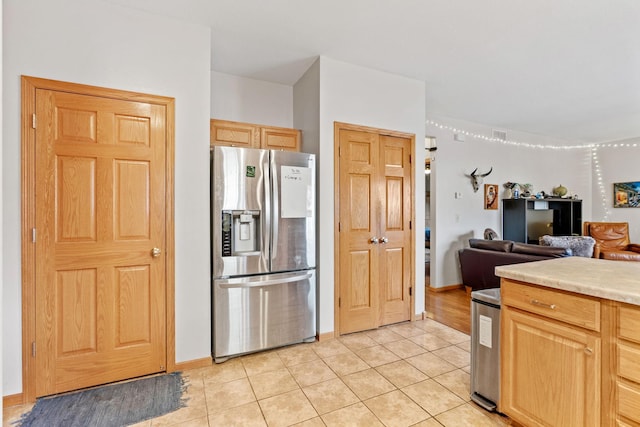 kitchen featuring light countertops, stainless steel fridge, light brown cabinets, open floor plan, and light tile patterned floors