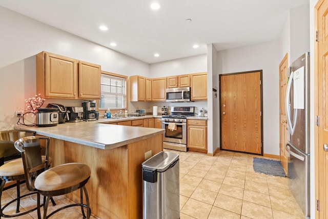 kitchen featuring a peninsula, a kitchen bar, recessed lighting, appliances with stainless steel finishes, and light brown cabinetry