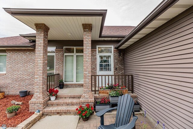 doorway to property with a porch, brick siding, and roof with shingles