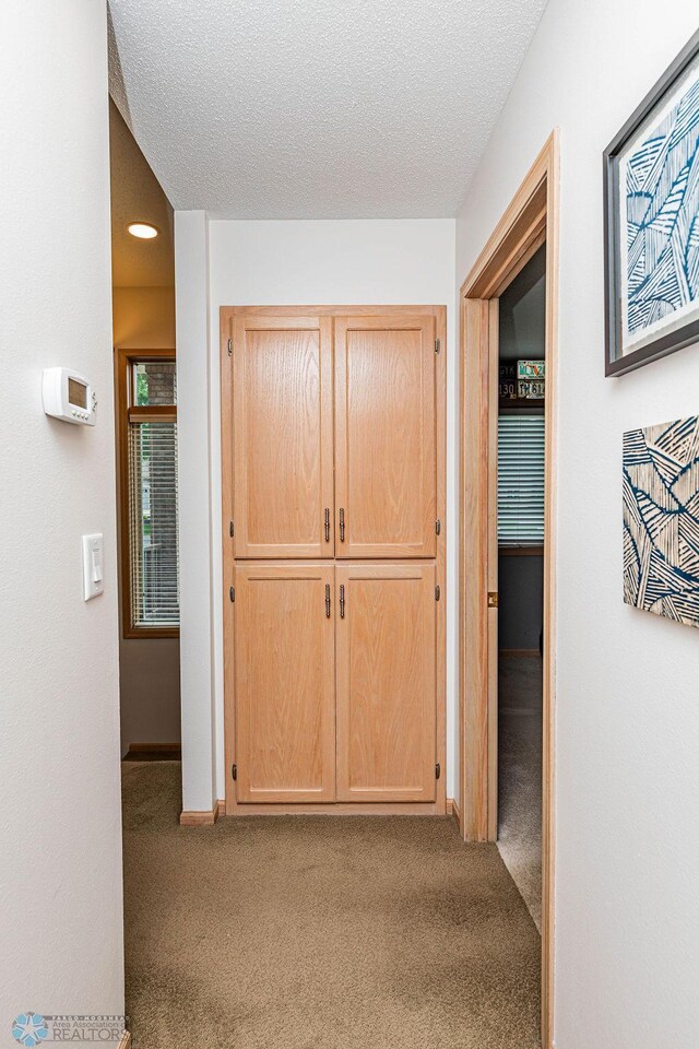 hallway with baseboards, carpet floors, and a textured ceiling