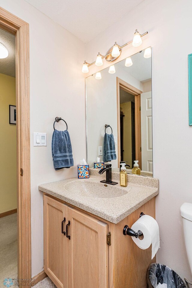 half bathroom with vanity, toilet, and baseboards
