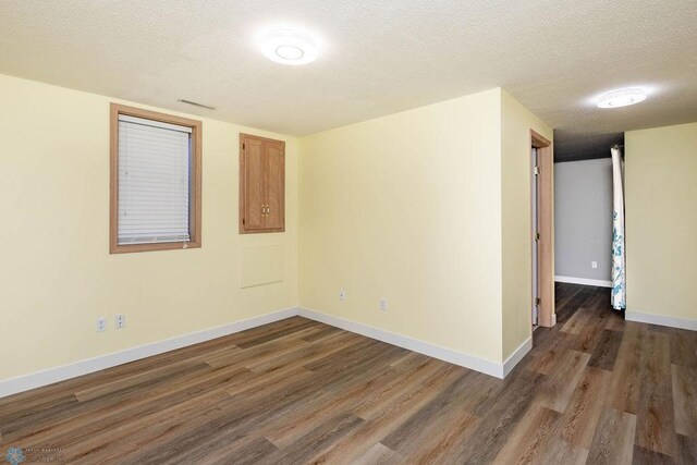 spare room with dark wood finished floors, visible vents, a textured ceiling, and baseboards