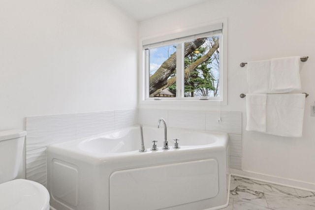 bathroom with marble finish floor, toilet, baseboards, and a garden tub